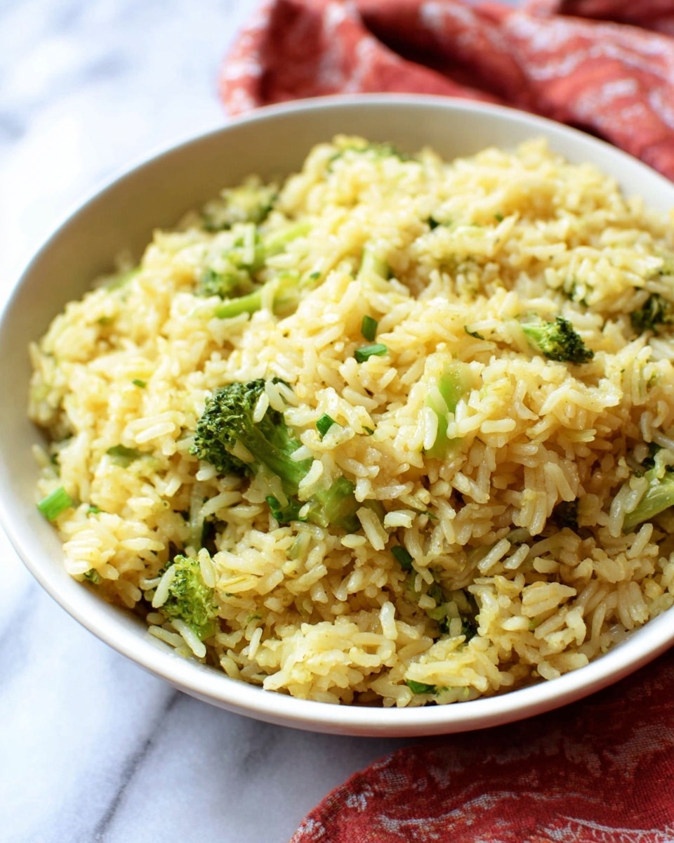 A white bowl filled with fluffy yellow rice mixed with small green broccoli pieces scattered evenly throughout. The rice grains look separate and soft, with some bits of broccoli florets and stems adding texture and color contrast. The bowl sits on a white marbled surface, with a red and white cloth partially visible underneath. The dish looks warm and freshly cooked, with steam gently rising from it. photo taken with an iphone --ar 4:5 --v 7