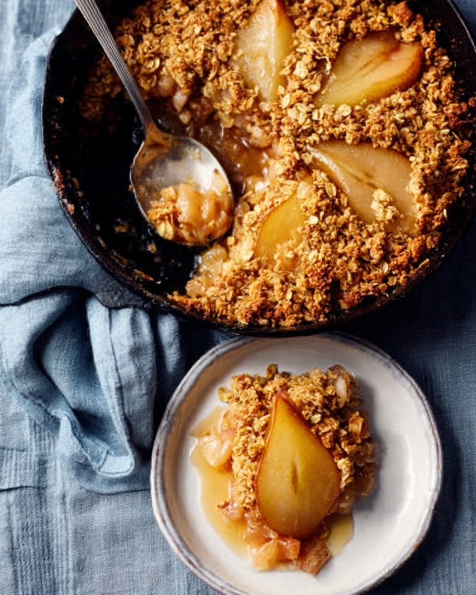 A cast iron pan holds a baked pear crumble topped with golden, crumbly oats and a layer of thick syrup with soft, brownish pear halves partially visible. A silver spoon scoops into the crumble, lifting a portion. Below the pan, a white plate with a single serving of the crumble sits on a blue-gray cloth surface with folded texture. The crumble serving looks moist and crunchy, with a light golden color and bits of tender baked pear. photo taken with an iphone --ar 4:5 --v 7
