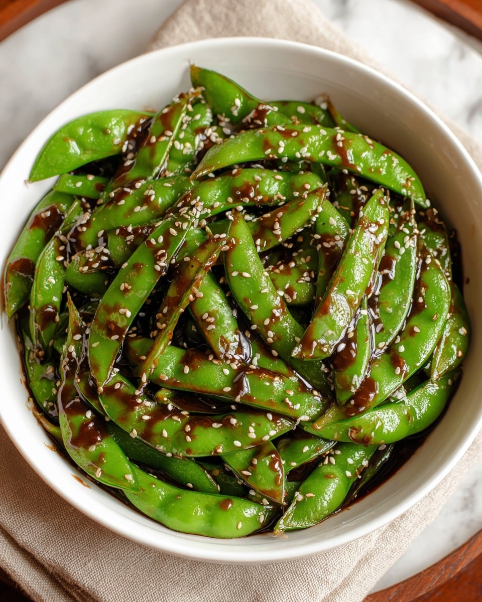 A white bowl filled with bright green sugar snap peas coated in a glossy dark brown sauce, with small white sesame seeds sprinkled evenly over the top, the peas have a fresh and slightly curved shape, all sitting on a beige cloth over a white marbled surface. photo taken with an iphone --ar 4:5 --v 7