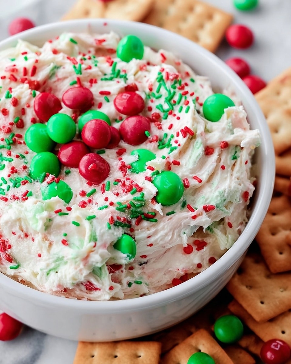 A white bowl filled with creamy white dip that has a soft, swirled texture, mixed with green and red small round sprinkles and larger green and red candy-coated chocolates on top. The bowl sits on a white marbled surface, surrounded by light brown rectangular crackers and round crackers. The red and green decorations are spread unevenly across the dip, giving it a festive look. photo taken with an iphone --ar 4:5 --v 7