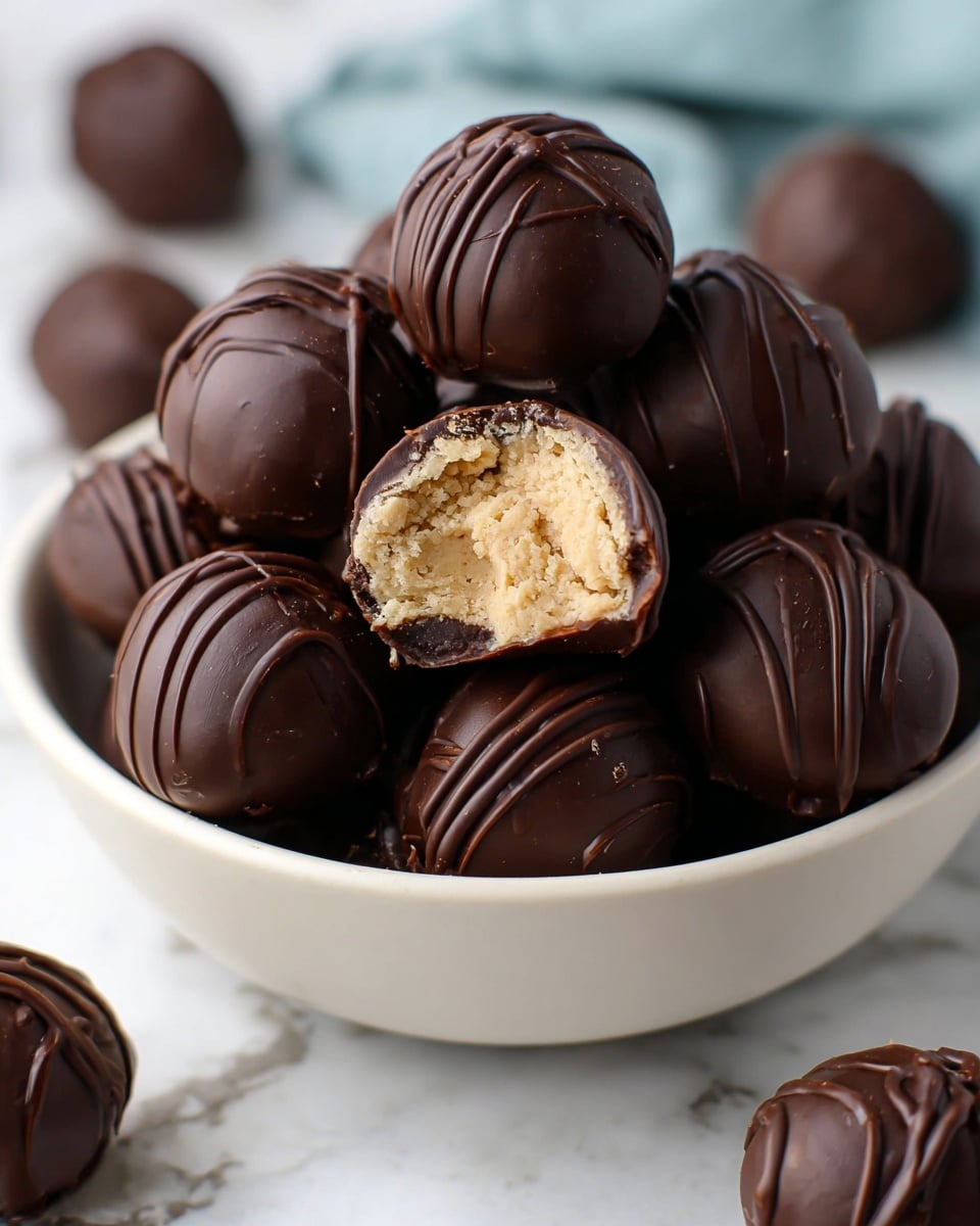 A white bowl filled with round dark chocolate truffles, each having a shiny smooth surface and thin darker chocolate drizzle lines on top, stacked closely. One truffle is cut in half and placed on top, revealing a light beige, slightly crumbly filling inside, contrasting with the dark outer shell. More truffles are scattered around the bowl on a white marbled textured surface, creating depth in the image. Photo taken with an iphone --ar 4:5 --v 7