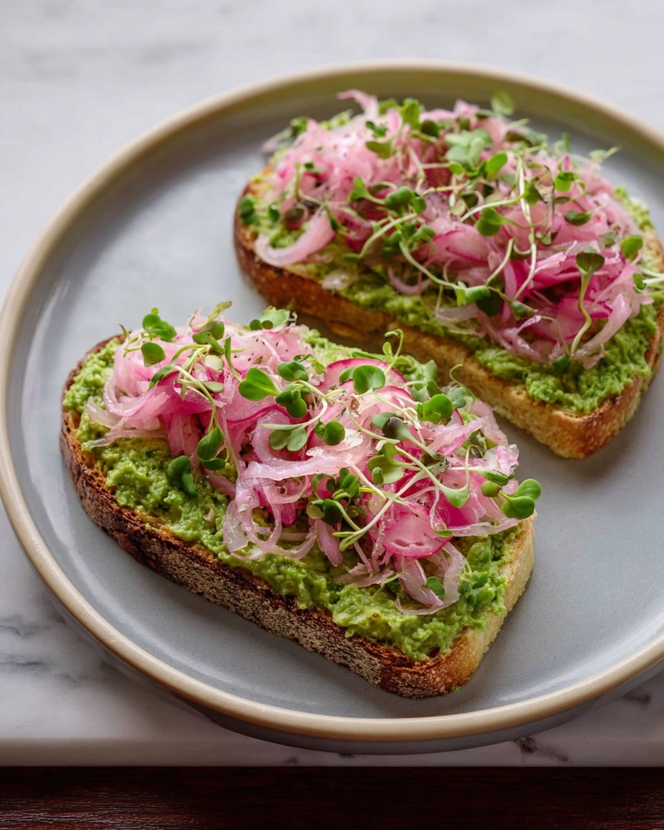 Two pieces of toast sit on a white plate with a light gray center, placed on a white marbled surface. Each slice has a thick layer of green spread with a slightly coarse texture. On top, there are loose, thin ribbons of light pink pickled onions, giving a soft, curly look. Scattered bright green microgreens with small leaves add freshness and a bit of height to the topping. The toast edges show a golden brown, crisp surface under the toppings. The overall look is fresh and colorful with a balance of green and pink tones. photo taken with an iphone --ar 4:5 --v 7