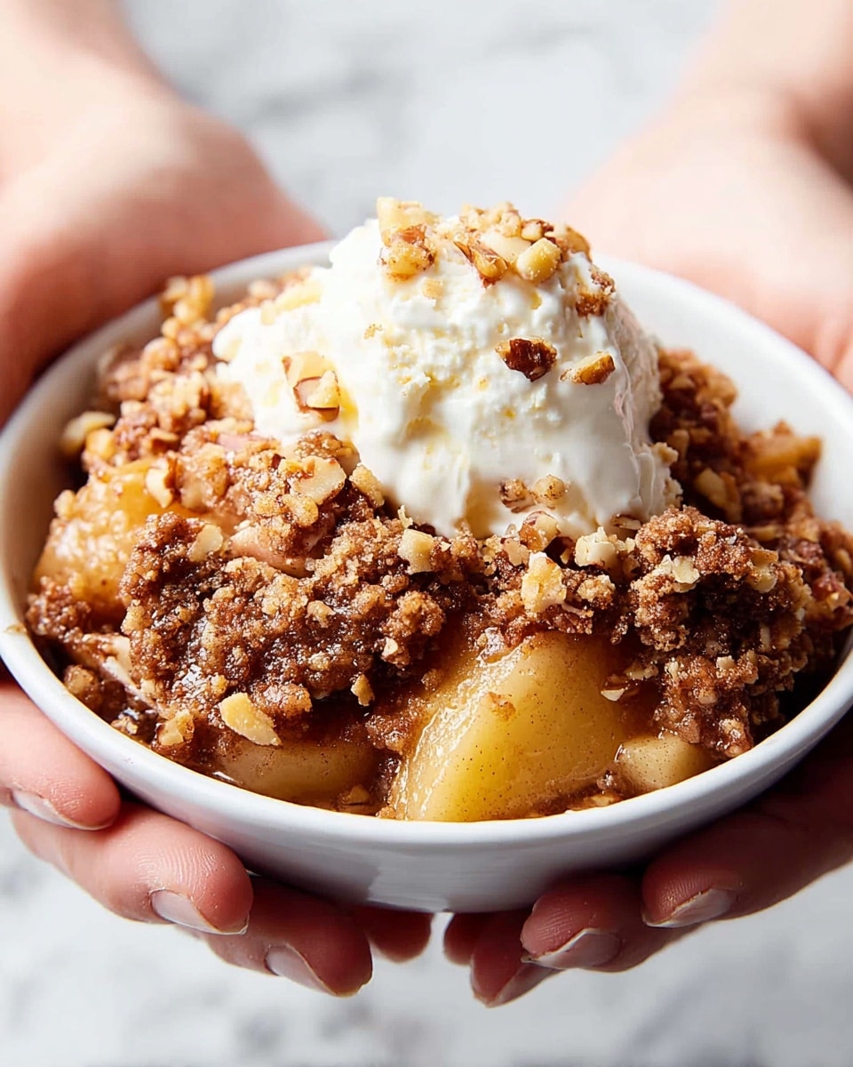 A close-up of a white plate holding a dessert with two main layers: the bottom layer is a chunky apple filling with soft, cooked apple slices covered in a coarse, crumbly, brown cinnamon topping, and the top layer is a creamy scoop of white ice cream sprinkled with small nut bits. The plate sits on a white marbled surface with some nut crumbs scattered around, and the background is a solid bright blue. photo taken with an iphone --ar 4:5 --v 7