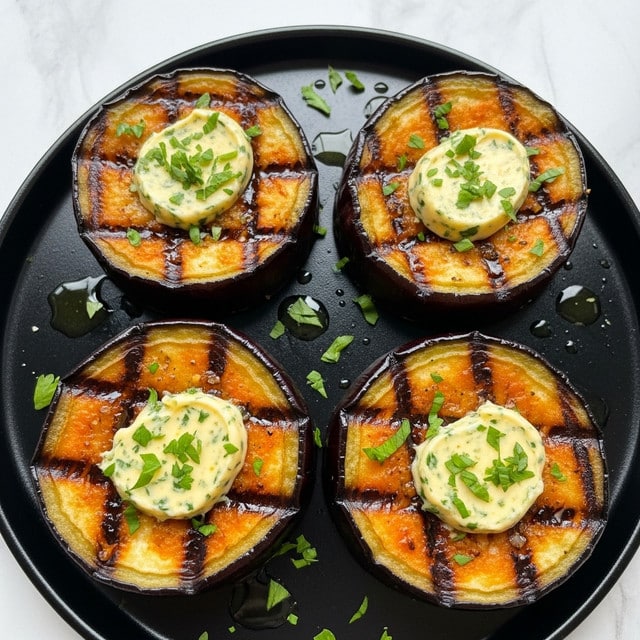 The image shows four thick slices of roasted eggplant arranged on a white marbled surface, each slice featuring a dark purple outer skin with a tender, golden-brown inner layer. On top of each eggplant slice, there is a generous dollop of creamy, light yellow garlic butter mixed with chopped green herbs, which add a fresh, speckled touch. The eggplant slices are glistening with oil, and small bits of herbs are scattered around the dish, enhancing the texture and color contrast. The close-up view highlights the crispy edges, the soft interior, and the melting garlic butter topping with a sprinkle of coarse salt visible on top. Photo taken with an iphone --ar 4:5 --v 7