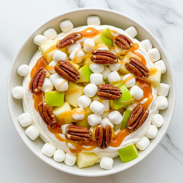 A white bowl filled with a fluffy base of whipped cream or a similar white creamy substance, topped with many small white marshmallows. Mixed in are light green apple chunks with smooth skin, and pieces of brown pecans scattered evenly across the top. Golden caramel sauce is drizzled loosely over everything, adding shine and contrast. The entire dish sits on a white marbled surface with a soft, natural light highlighting the textures and fresh colors. photo taken with an iphone --ar 4:5 --v 7