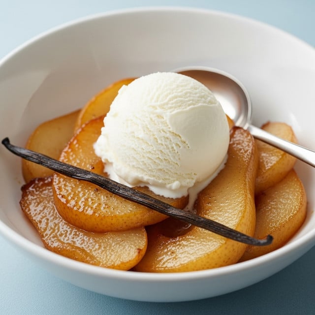 A white bowl holds a warm dessert with multiple layers: the base consists of caramelized, golden-brown cooked pear slices with a soft, slightly shiny texture, accompanied by a vanilla bean pod for added detail. On top sits a single scoop of smooth, creamy vanilla ice cream, its pale white color contrasting with the caramel tones beneath. A silver spoon rests inside the bowl, angled towards the front, ready to scoop the dessert. The bowl is placed on a light blue surface, which is softly blurred to keep focus on the dish. Photo taken with an iphone --ar 4:5 --v 7