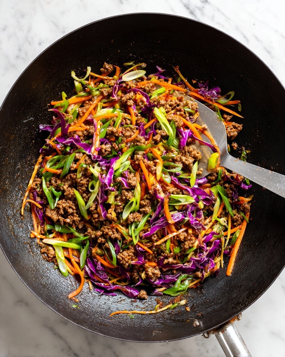 A large black wok filled with a colorful mix of stir-fried ingredients including cooked ground meat, thinly sliced purple cabbage, orange carrot strips, and light green cabbage pieces. The dish is sprinkled with sliced green onions on top, adding a fresh contrast. A metal spoon rests in the wok, partially scooping the mixture. The background is a white marbled texture. photo taken with an iphone --ar 4:5 --v 7