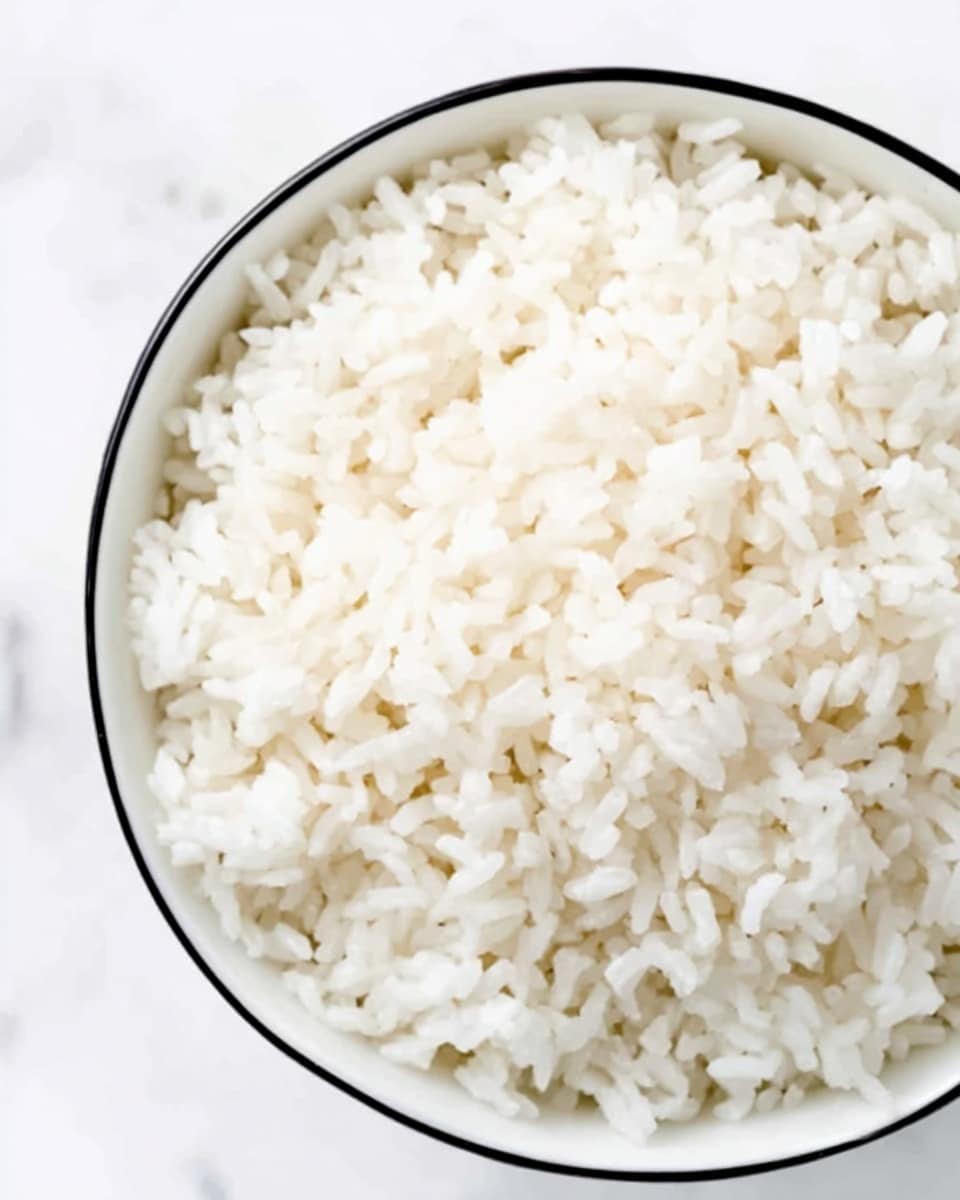 The image shows a close-up of plain white rice inside a white bowl with a thin black rim. The rice grains appear soft and fluffy, tightly packed to fill the bowl evenly. The background is a white marbled surface. The scene is simple, focusing just on the texture and color of the rice. Photo taken with an iphone --ar 4:5 --v 7