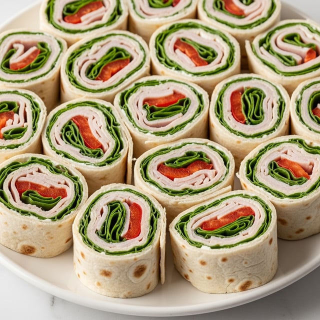 A white plate filled with several small tortilla pinwheel sandwiches, each cut into bite-sized rounds. Each pinwheel has visible layers starting with a light beige tortilla wrap, followed by bright green leafy spinach, slices of orange carrot strips, creamy white cheese, and light pink turkey or ham, all neatly rolled and sliced. The pinwheels are arranged close together, with some showing the fresh textures of the vegetables and cheese. The plate sits on a white marbled surface. photo taken with an iphone --ar 4:5 --v 7