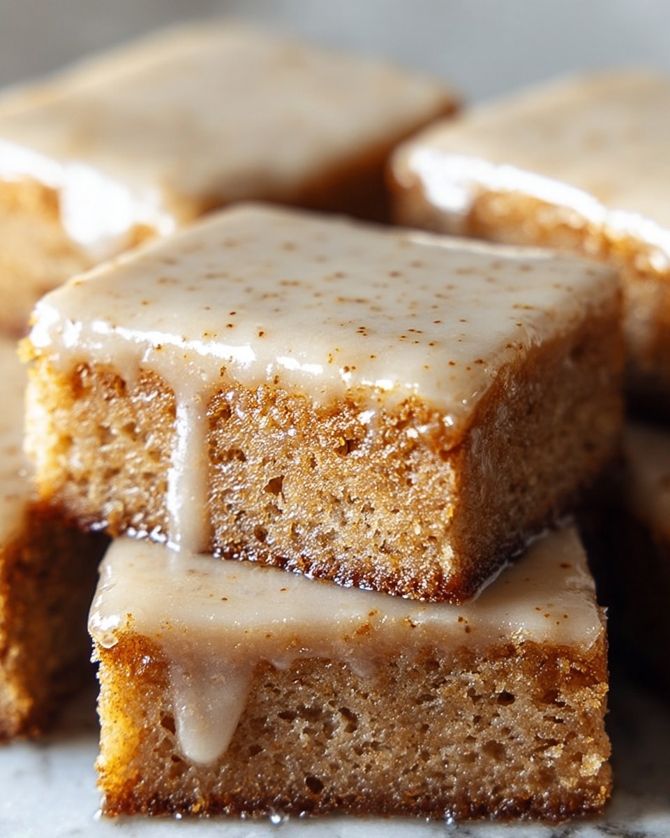 The image shows four close-up square pieces of a moist, light brown cake with a smooth, creamy glaze on top. Each piece has two visible layers: a dense, textured cake base in a rich brown shade with tiny crumbs around the edges, and a thick layer of shiny, speckled beige glaze covering the top fully, dripping slightly down the sides. The background is a white marbled texture that highlights the warm colors of the cake pieces. Photo taken with an iphone --ar 4:5 --v 7
