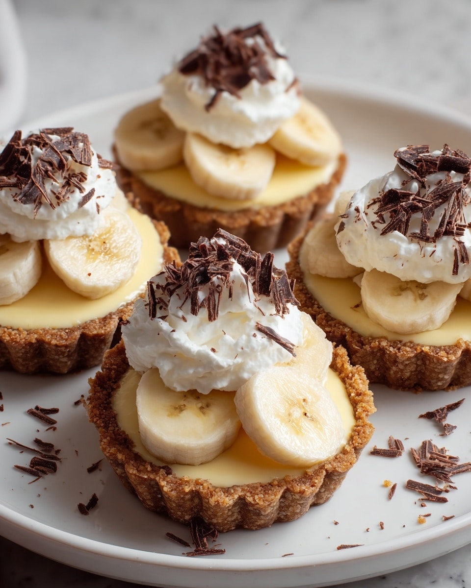 Four small tartlets sit on a white plate placed on a white marbled surface. Each tartlet has a crumbly golden-brown crust as the base, followed by a smooth light cream layer. On top of the cream, there are sliced banana pieces arranged in a circle. Above the bananas, there is a fluffy white whipped cream layer, sprinkled with dark chocolate shavings that add texture and contrast. Photo taken with an iphone --ar 4:5 --v 7