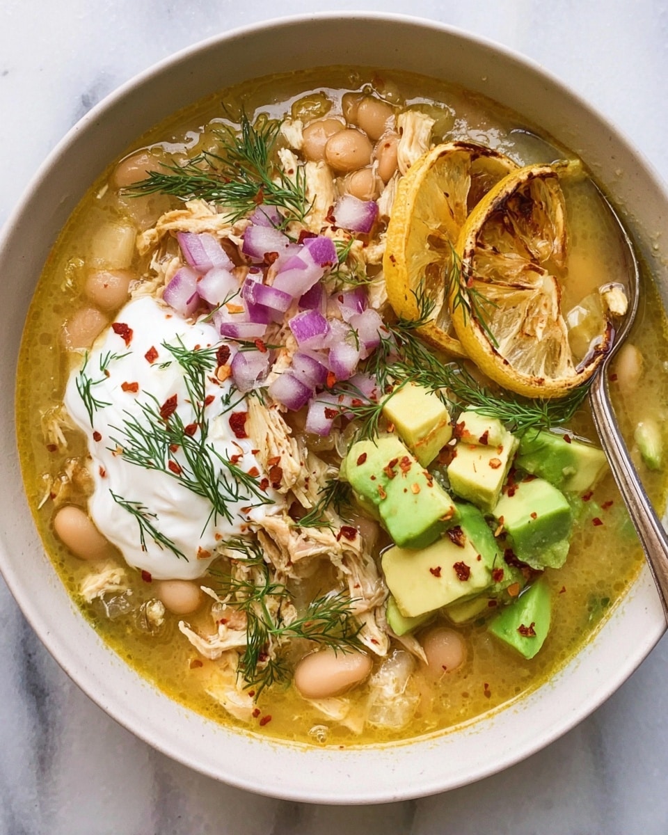 A white bowl filled with a golden broth soup base with visible beans and shredded chicken. On top, there are layers of diced purple onions in the center, avocado chunks on the right, and yellow lime wedges near the top, all sprinkled with red chili flakes. White creamy dollops are on the right side of the bowl. Fresh green dill sprigs are scattered across the dish, adding a touch of vibrant color. A silver spoon rests inside the bowl, with its handle extending outward. The bowl is placed on a white marbled textured surface. photo taken with an iphone --ar 4:5 --v 7