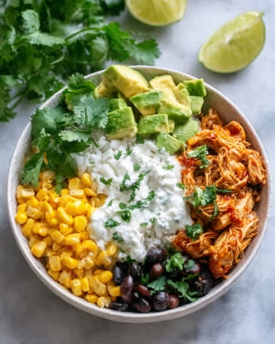A white bowl on a white marbled surface contains a colorful layered dish. The bottom layer is white rice topped with bright orange shredded chicken on the bottom right side. To the top right, there is a neat pile of yellow corn kernels. The top left side has sliced green avocado pieces, and fresh green cilantro leaves are scattered on the top left and bottom right edges. In the center, a dollop of white creamy sauce sits over the rice and chicken. A wedge of lime and some blurred greens are visible in the background. Photo taken with an iphone --ar 4:5 --v 7