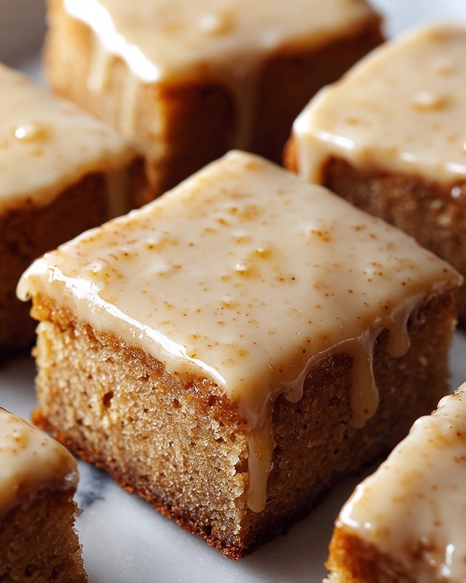 Close-up of four thick square pieces of cake with two visible layers: the bottom layer is a moist, light brown cake textured with small air holes, and the top layer is a smooth, creamy glaze with a light beige color and small darker specks evenly spread. The glaze appears slightly shiny and drips gently over the edges of the cake, giving a fresh, glossy look. The pieces are arranged close together on a white marbled surface. photo taken with an iphone --ar 4:5 --v 7
