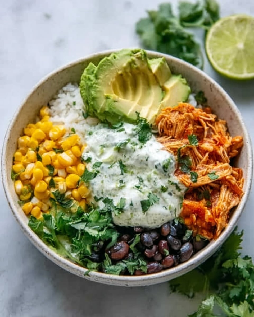 A white bowl filled with a colorful grain bowl on a white marbled surface. The bowl has neat sections: bright yellow corn on the top right, fresh green avocado slices on the top left, shredded orange chicken mixed with black beans on the bottom right, and white rice in the middle. A dollop of white creamy sauce with green herbs sits on top of the rice. Fresh cilantro is placed on the sides, and a lime wedge is seen in the background. The photo taken with an iphone --ar 4:5 --v 7