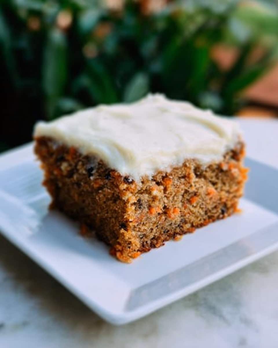 A square piece of carrot cake with two layers is on a white square plate. The bottom layer is a light brown cake speckled with small dark bits, showing a moist and soft texture. The top layer is a thick, creamy white frosting evenly spread, smooth and slightly shiny. The cake piece is centered on a white marbled surface with some green blurry plants in the background. Photo taken with an iphone --ar 4:5 --v 7