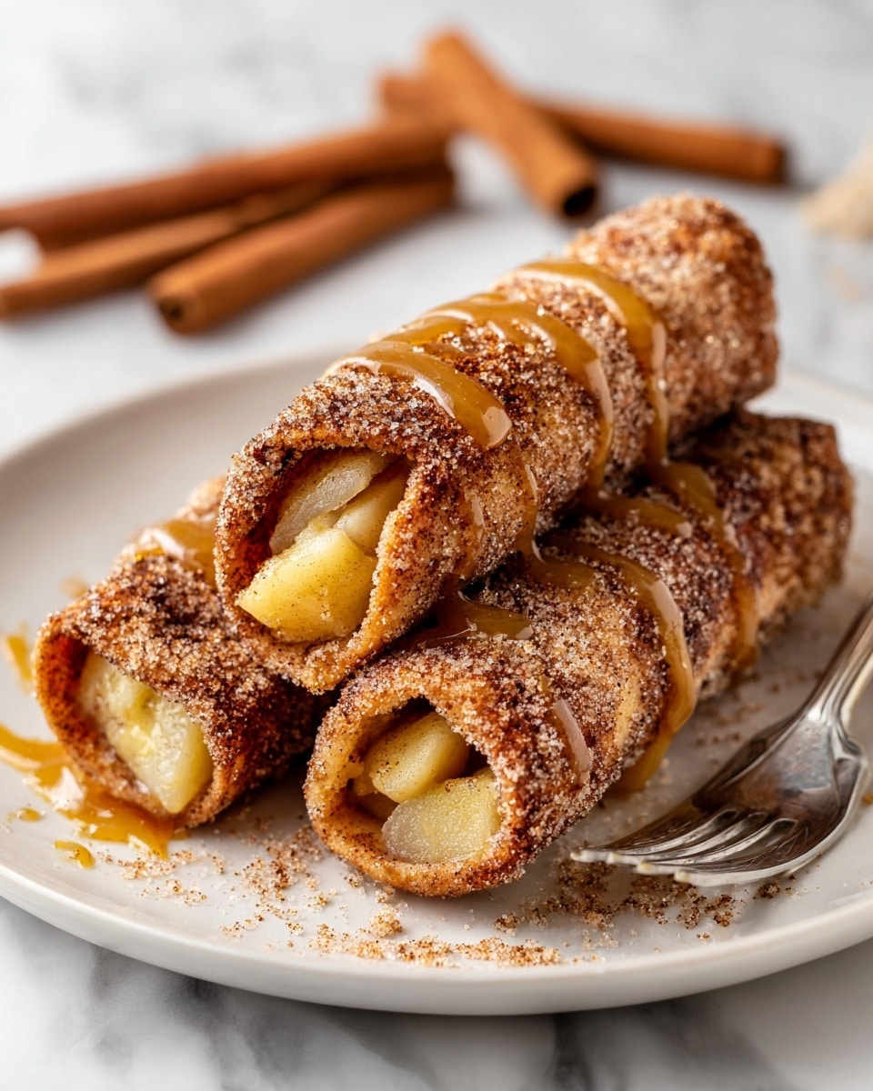 The image shows a white plate with three rolled pastries closely stacked, each coated with a layer of cinnamon sugar that gives a grainy texture and light brown color on the outer surface. Inside each roll is a soft, translucent, and slightly gooey apple filling visible at the open ends, showing a mix of pale yellow and light brown colors. There is a drizzle of golden caramel sauce over the top of each roll that adds a shiny, sticky layer to the cinnamon sugar. A silver fork rests on the plate behind the pastries, all set on a white marbled surface, and cinnamon sticks are blurred in the background. Photo taken with an iphone --ar 4:5 --v 7