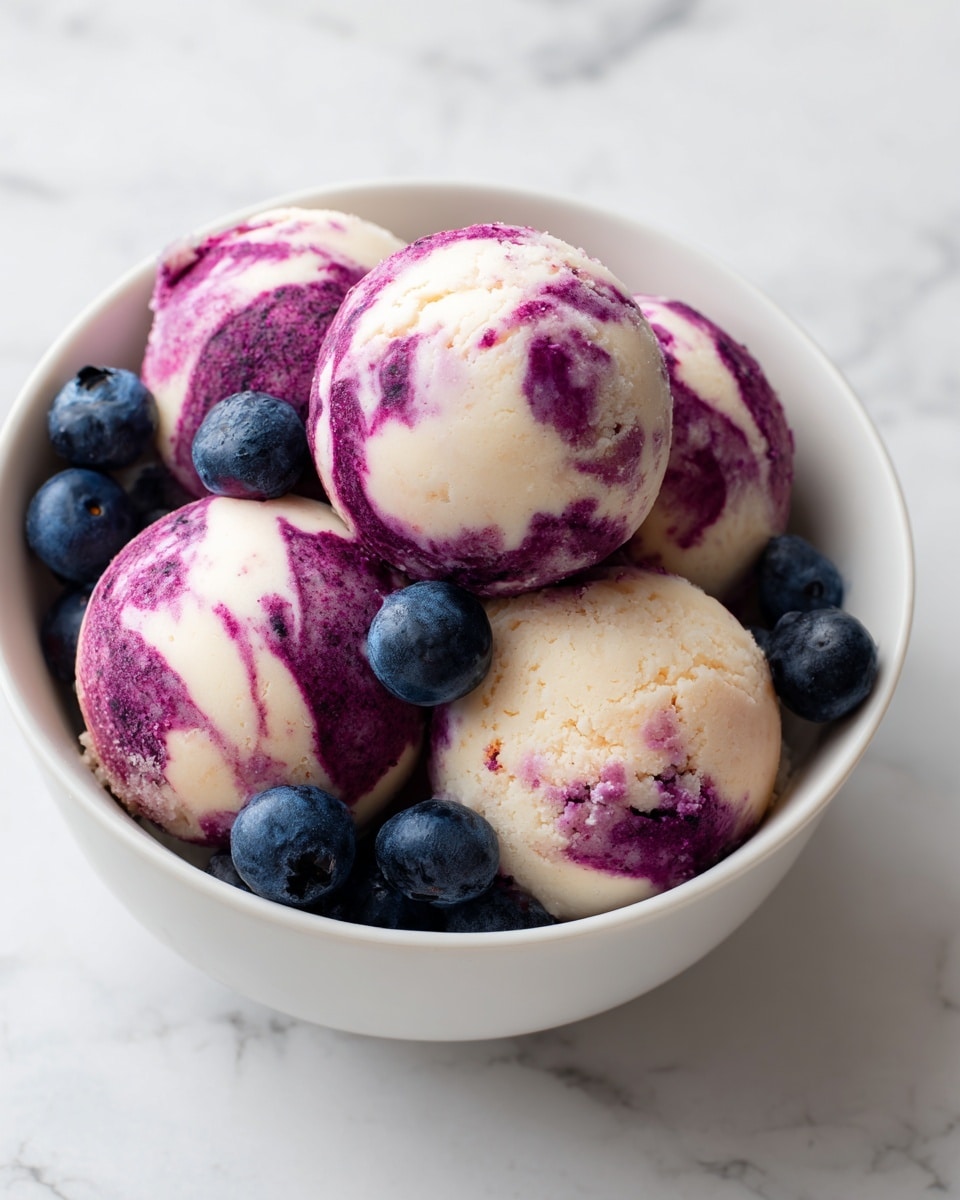 The image shows a white bowl filled with five round, creamy balls that have a marbled purple and white color, indicating a mixture of flavors or ingredients. Around the balls, a few fresh blueberries rest, adding a deep blue contrast to the dish. The balls have a smooth but slightly uneven texture with visible purple streaks flowing through the creamy white base. The bowl sits on a white marbled surface, making the colors stand out clearly. Photo taken with an iphone --ar 4:5 --v 7
